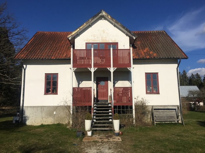 Slitet reveterat hus från 1900-talet med liten veranda och balkong.