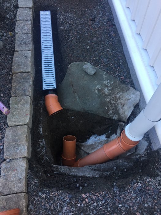 Nedlysta rännor och stuprör vid husgrund med grus och stenar, redo för vattenavledning.