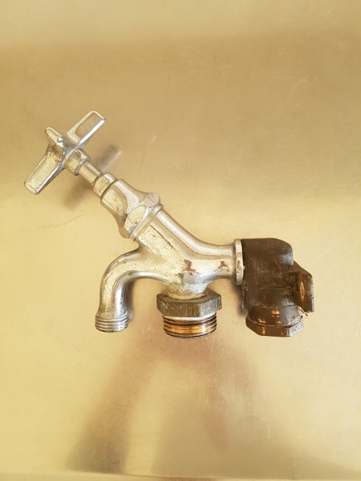 Gammal silverfärgad vattenkran med korsformigt handtag och svart PRK-koppling.