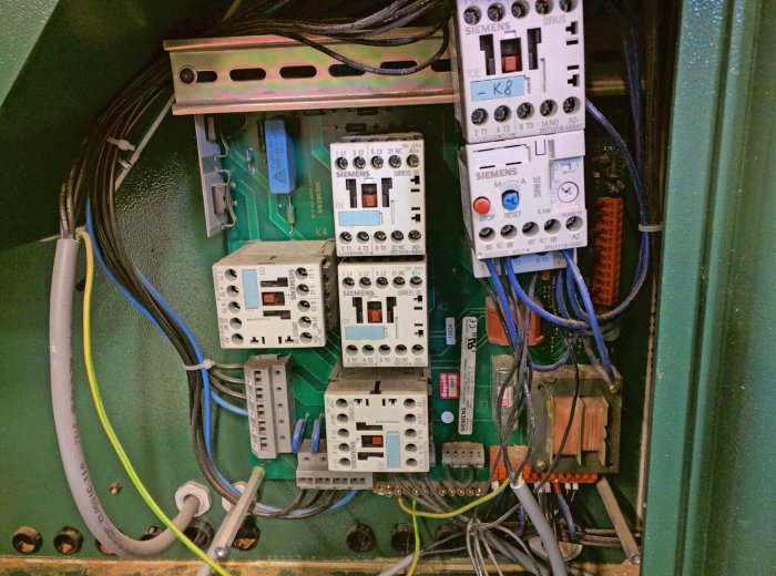 Interiör av en elektrisk kontrollpanel med diverse Siemens kretsbrytare, reläer och ledningar.