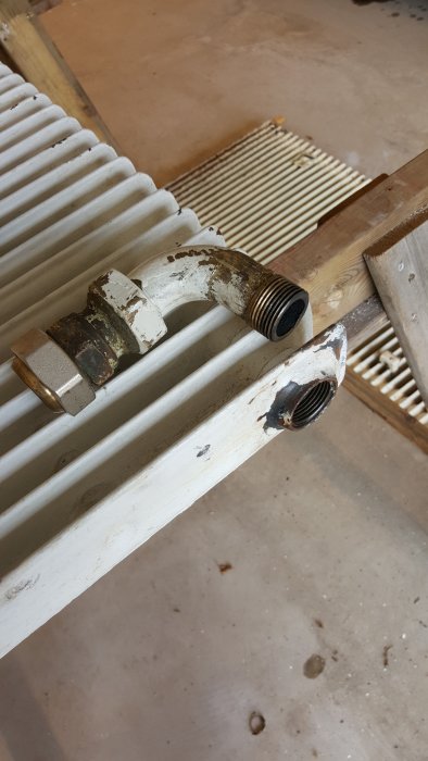 Radiatorkoppling med gängad del och mutter, nötta ytor, i en verkstadsmiljö.