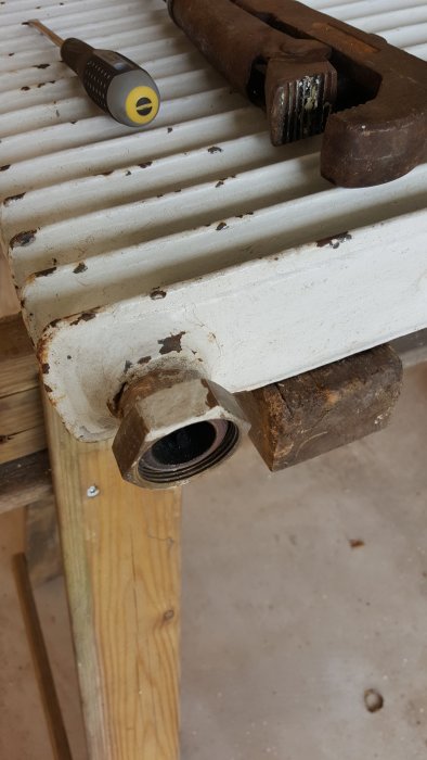 Radiator med borttagen mutter, rörtång och skruvmejsel på ett trästycke.