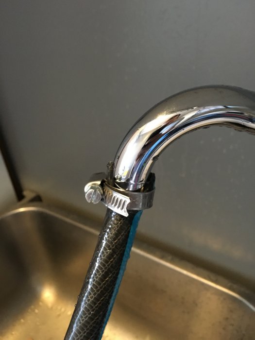 En slang ansluten till kökskran med hjälp av en slangenhet och gängtejp, omgiven av ett kök.