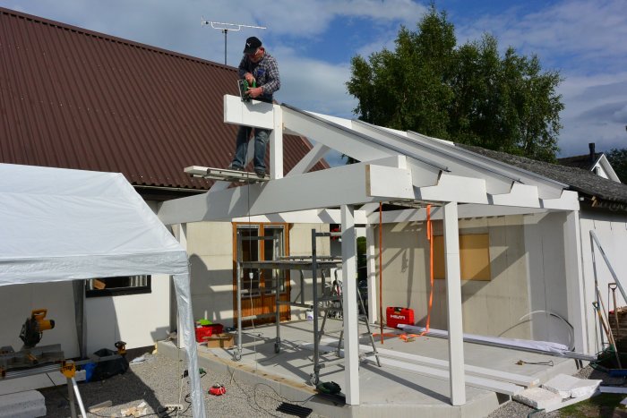 Byggarbetsplats med person som arbetar på takkonstruktion av limträ för skjutdörrar.