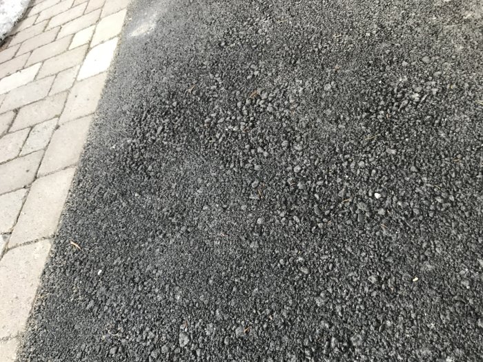 Ny lagd asfalt med större stenar nära kanten och finare textur i mitten, intill marksten.