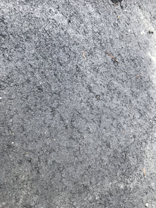 Nybelagd asfalt med synliga större stenar och några lösa smårisslor.