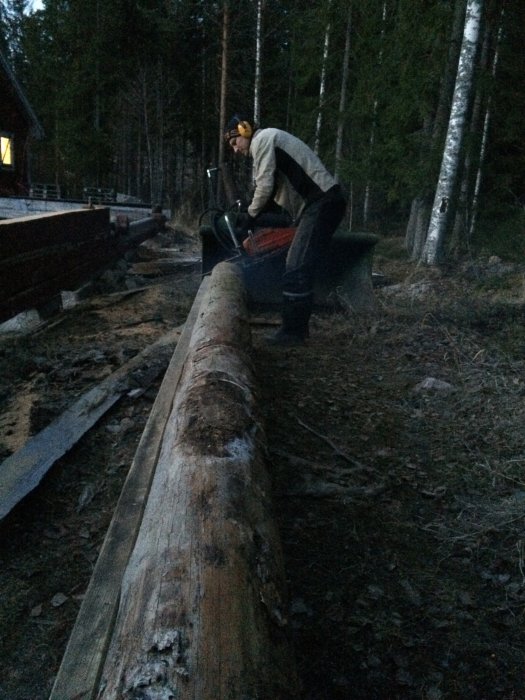 Person arbetar med att såga till en stor stock vid skymningen.