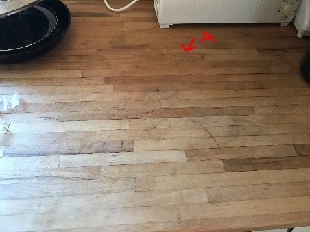 Träbänkskiva med vattenskador och synlig fukt i skarven betecknad med en röd pil.