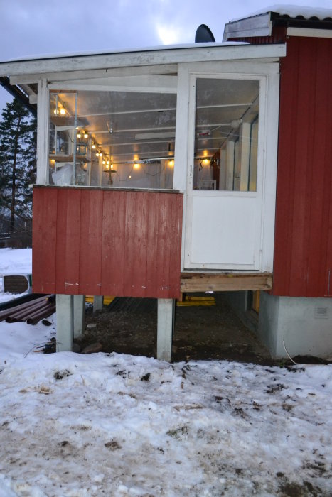 Ett uterum på pelare avslöjat utan trappa med snötäckt mark och konstruktionsmaterial i förgrunden.