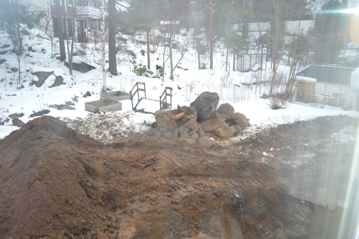 Uppgrävd trädgård med jordhögar under vinter för dräneringsarbete, synligt snötäckt landskap i bakgrunden.