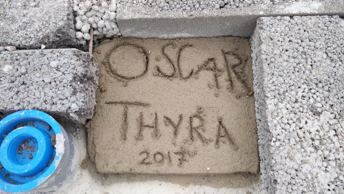 Färsk betong med barnens namn "OSCAR THYRÅ 2017" ingraverat, bredvid lecablock och blå flexslang.