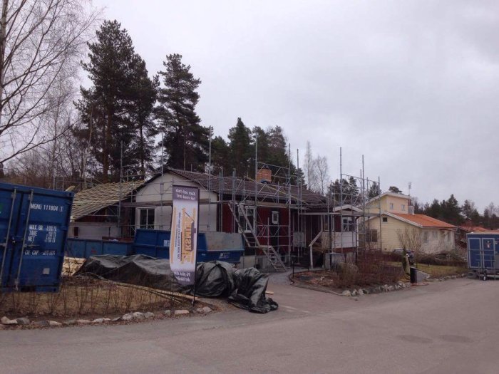 Hus under renovering med ställningar, delvis pålagd läkt och byggmaterial framför.