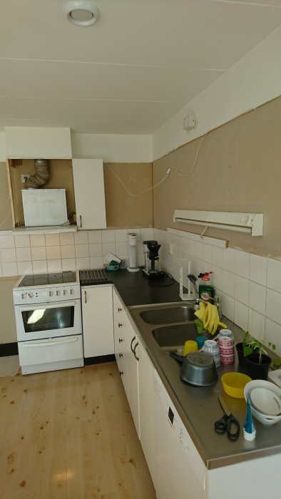 Kök under renovering med borttagna överskåp, kakelvägg och äldre vitvaror.
