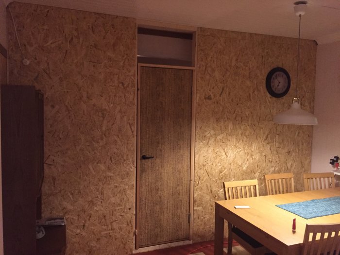 Vägg i matrum täckt med OSB-skivor med en tillfällig dörr under renovering.