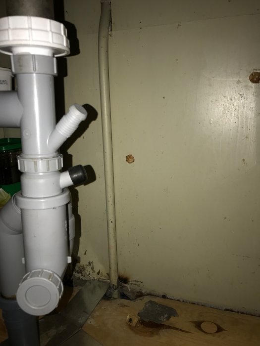 Gammalt järnrör för kallvatten och vattenlås under diskbänk i kök med planer på diskmaskinsinstallation.