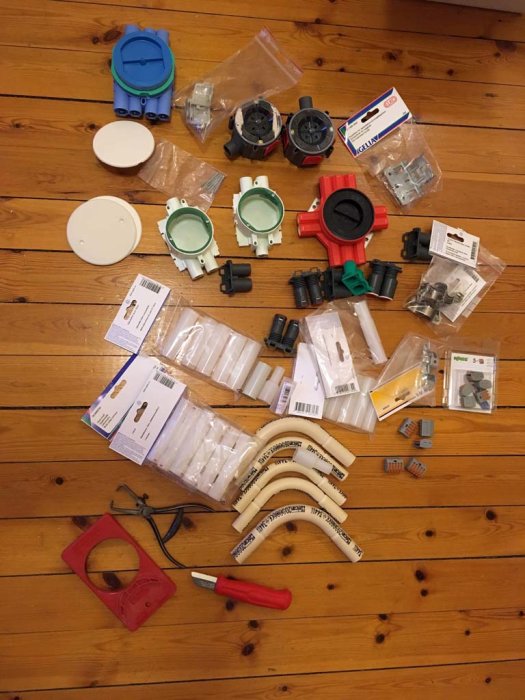 Överblivet elinstallationsmaterial såsom dosor, rör, kopplingar och verktyg utspridda på trägolv.