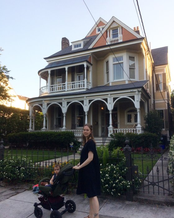 Kvinna med barnvagn framför ett traditionellt hus i New Orleans vid solnedgången.