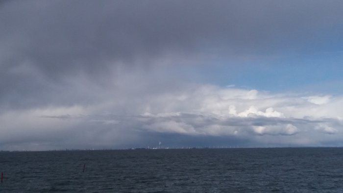 Utsikt över havet med mörka moln ovanför horisonten och synliga vindkraftverk i fjärran.