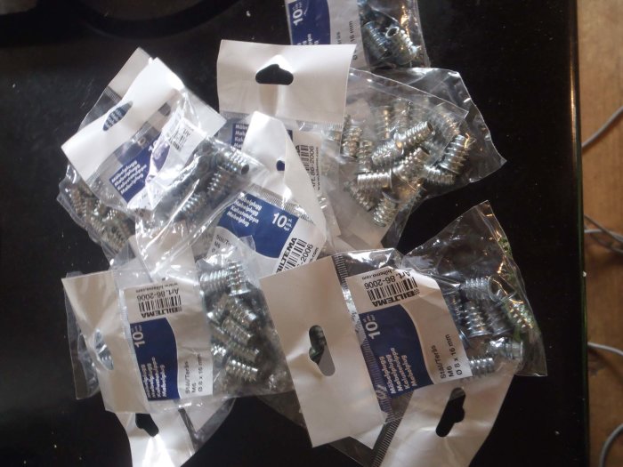 Flera förpackningar med skruvar utspridda på en mörk yta.
