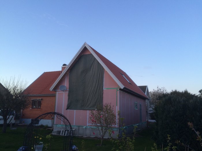 Ett hus under renovering med presenning och byggnadsställningar mot en klar himmel.