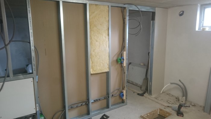 Renoveringsarbete med isoleringsmaterial i väggstomme och synlig rördragning i ett rum under ombyggnad.