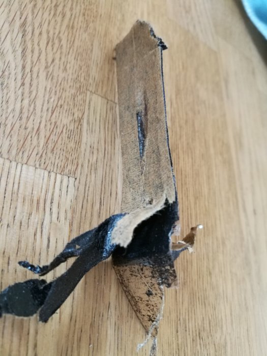Äldre byggmaterial med flerskiktad struktur och plastlager, riven kant visar lagerindelningen.