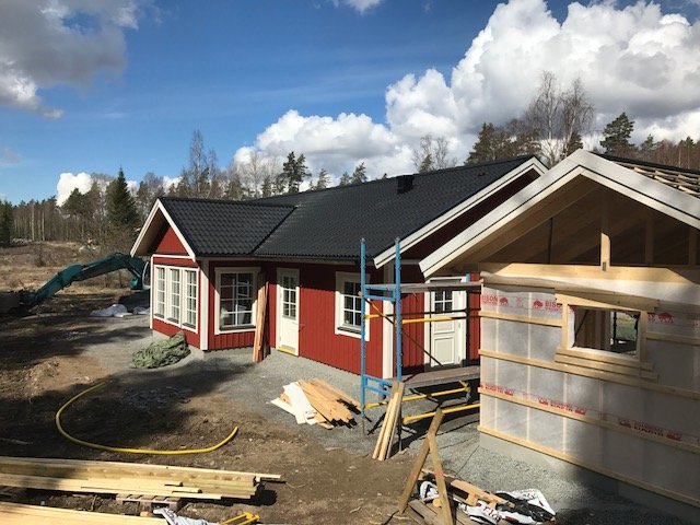 Nybyggt hus med rött tegel och svart tak, synlig isolering och carport under konstruktion.