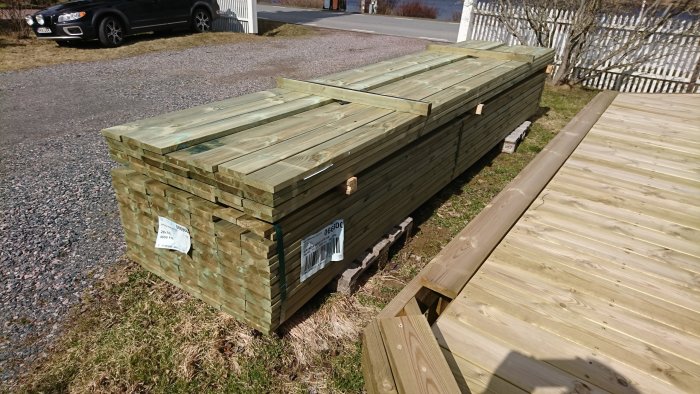 Stapel med ny trall bredvid redan lagd trall på en solbelyst gård.