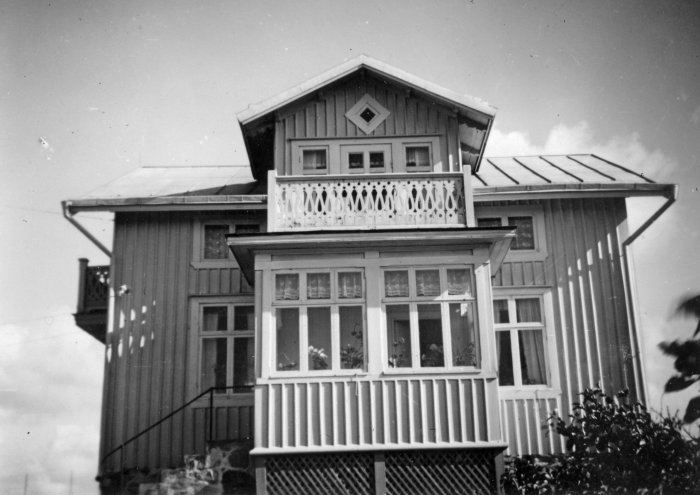 Svartvit bild av äldre hus med veranda och nästan platt tak som kan behöva ventilering vid utbyggnad.