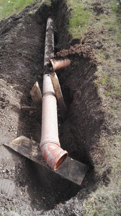 Avloppsrör i grävd dike med läckage vid skarv, stöttat av improviserad träställning.