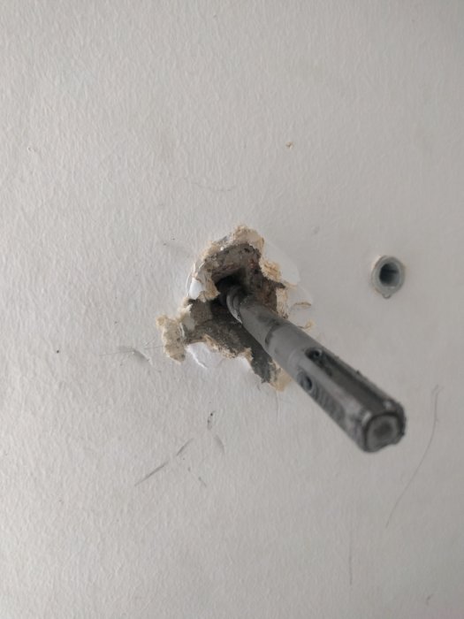 Borr fastnar i betongvägg, omringad av oregelbundet borrspån och skadat område.