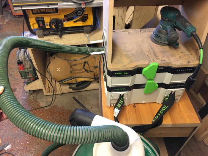 Verkstad med en Festool dammsugare och cyklon, kopplade med en sugslang, bredvid en slipmaskin och en Dewalt såg.