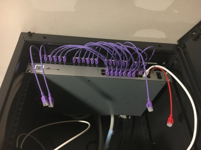 Nätverksswitch i skåp med anslutna Ethernet-kablar, huvudsakligen lila, en röd och en vit.