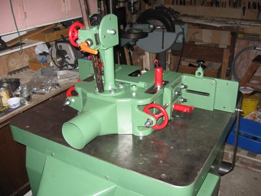 Nymålad grön industriel maskin på ett arbetsbord i en verkstad med verktyg och material i bakgrunden.