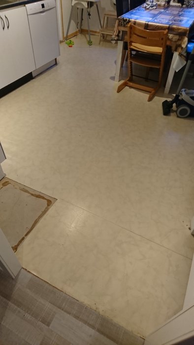 Ett halvt avlägsnat laminatgolv i kök med en synlig dammsugare och köksmöbler i bakgrunden.