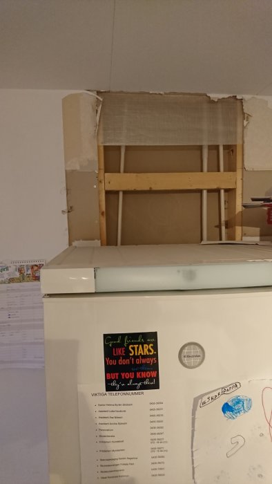 Renovering i kök med halvavlägsnad gipsskiva bakom kylskåp och synligt trästomme.