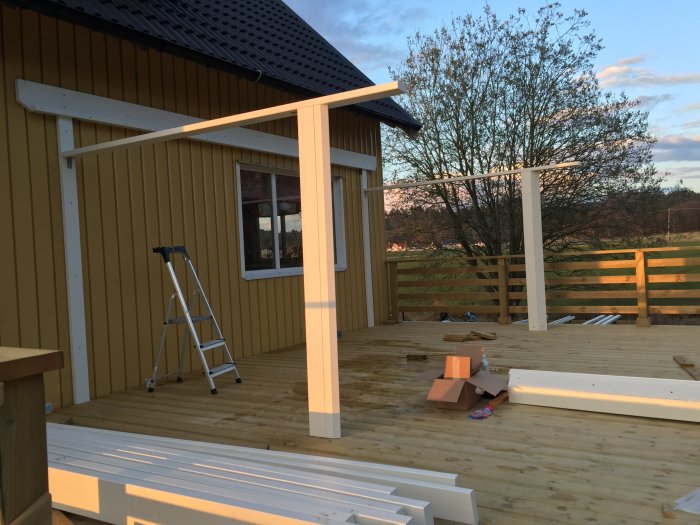 Uppförande av vita skärmtaksstolpar på en terrass med byggmaterial och stege.