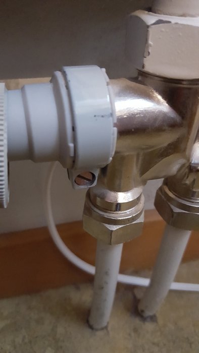 Avbrutet vitt termostatvred på en radiator med klämkoppling synlig.