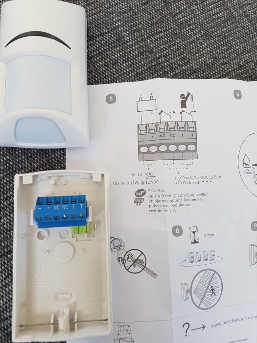 Öppen elektronikenhet med blå terminalblock bredvid en instruktionsmanual som visar kabelanslutningar.