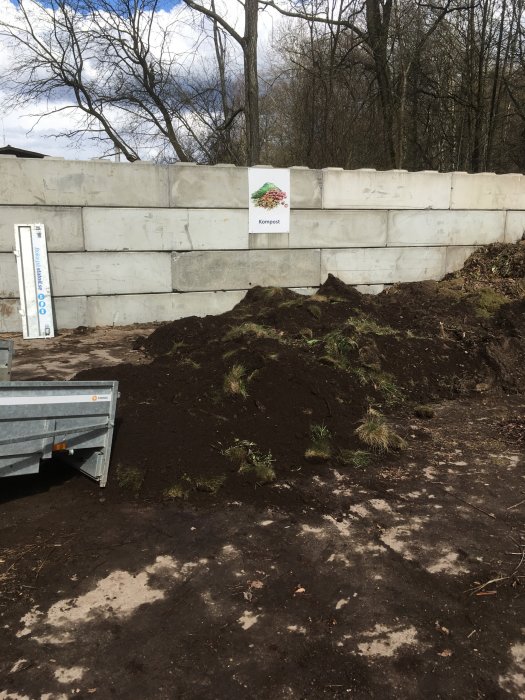 Nygrävd odlingshörna med upphöjd betongvägg i bakgrunden och en släpvagn intill en hög med jord.