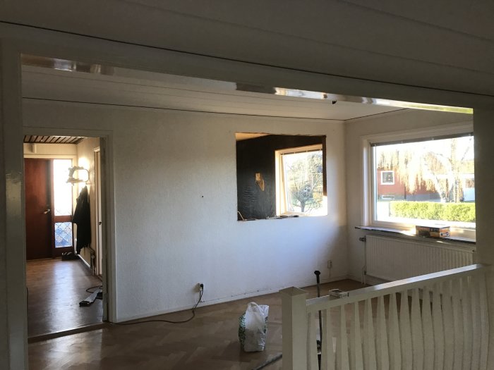 Interiör av ett rum under renovering med en nygjord öppning i väggen och utsikt mot ett fönster.