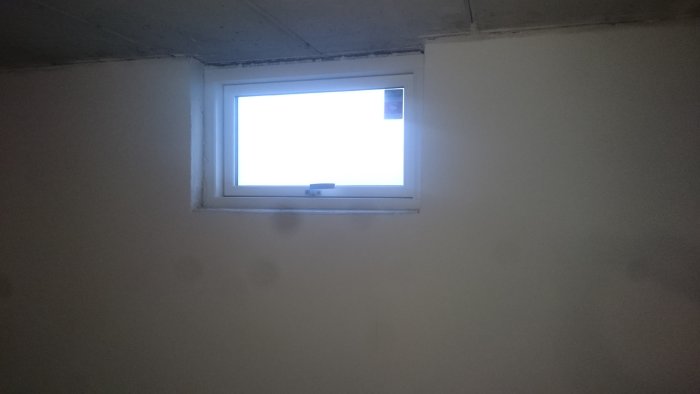 Nytt installerat fönster med aluminiumram och frostad glasruta i en nyspacklad och gipsad vägg.