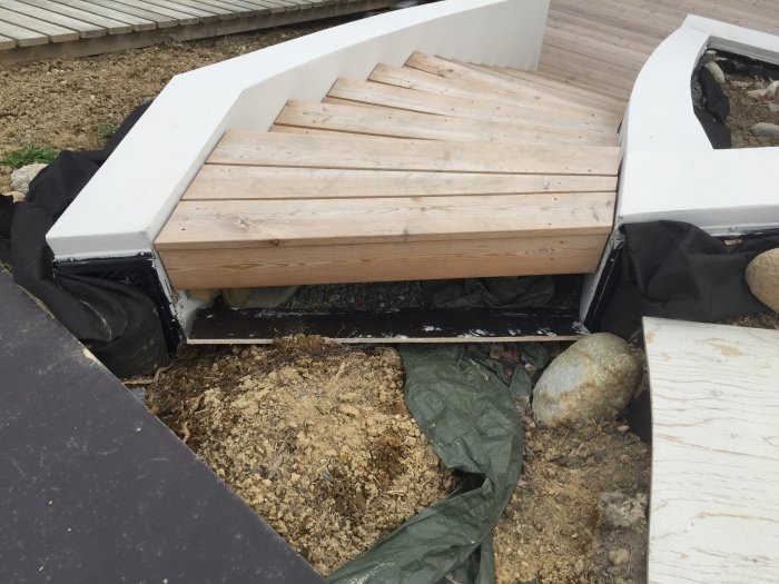 Trätrappa under konstruktion med vit sarg och synlig svart markduk samt omliggande byggmaterial.