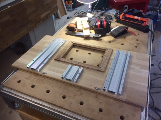 Fräsbord under konstruktion med aluminiumprofiler och trädetaljer på en verkstadsbänk med verktyg i bakgrunden.