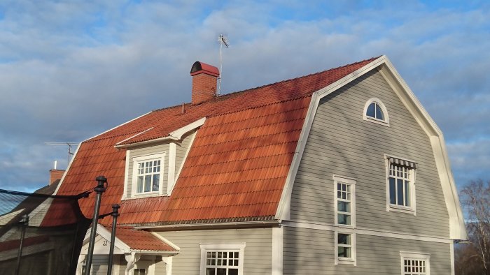 Tvåvåningshus med brutet tak och vita fönster mot en blå himmel.