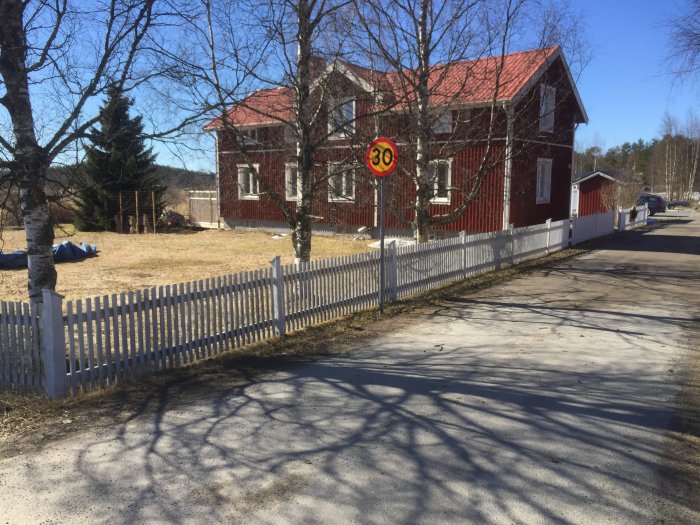 Vitt staket med skador framför ett rött hus och hastighetsskylt som visar 30 km/h.