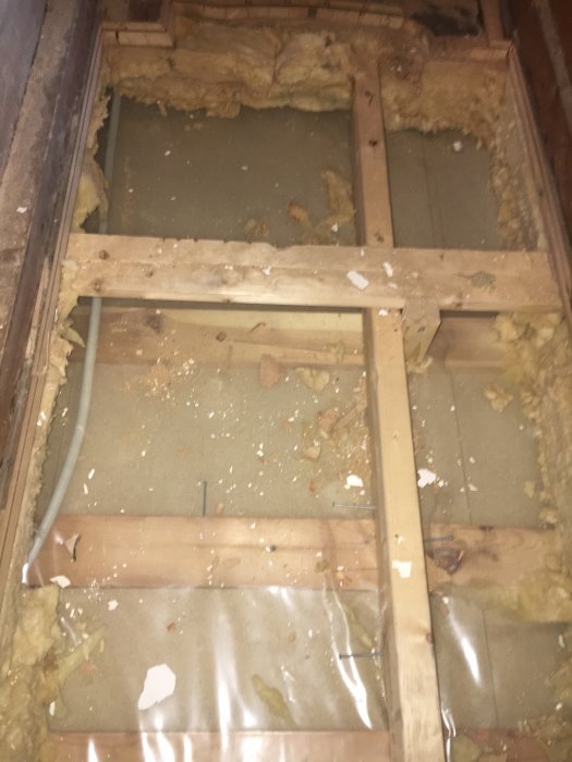 Golvbjälklag med isolering, genomskinlig plast, spillror och smuts, osammanhängande syn av byggstrukturens insida.