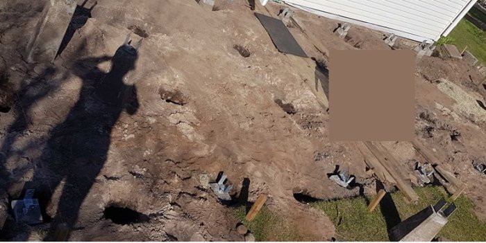 Uppgrävd trädgård för altanbygge med synliga hål och några plintar i sandig jord.