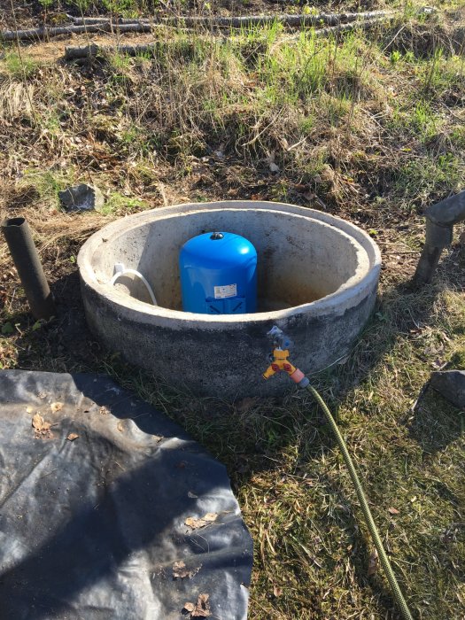 Gammal brunn med nyinstallerad hydropress och tappkran, kopplad till slang ute i ett soligt gräsområde.