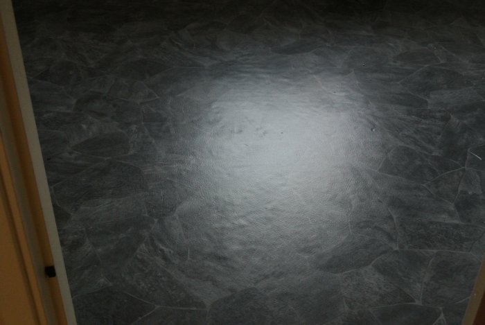 Ojämn och vågig badrumsmatta med skada verkar smält av byggfläkt.